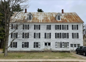 The North Conway House or Bunker Building is a large, three-story wood-frame building with a weathered white facade and black shutters. A steep pitched metal roof is showing rust and wear.