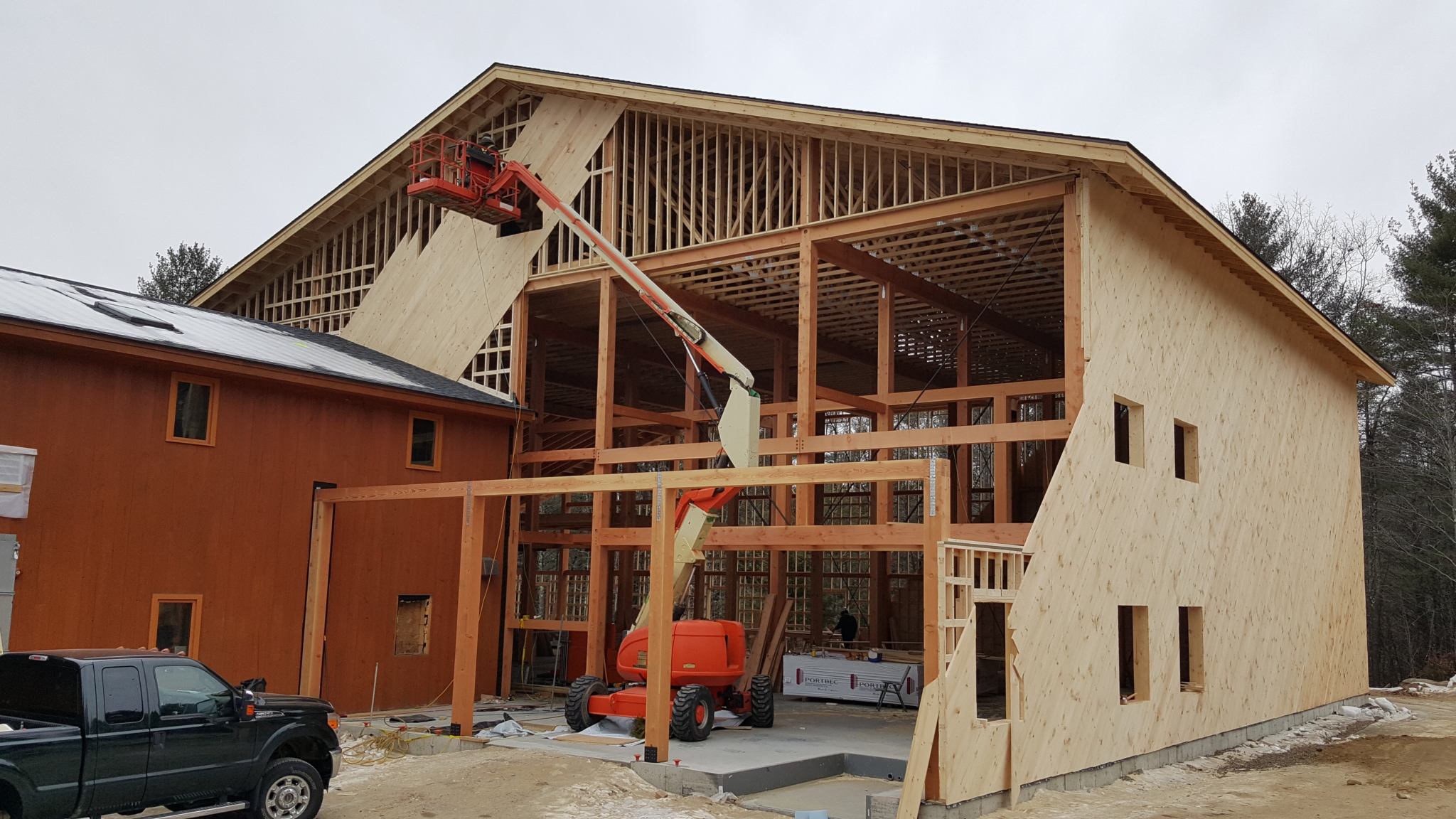 During winter, as there is snow on the ground and around the building, construction workers continue to frame a large commercial building while utilizing a scissor lift.