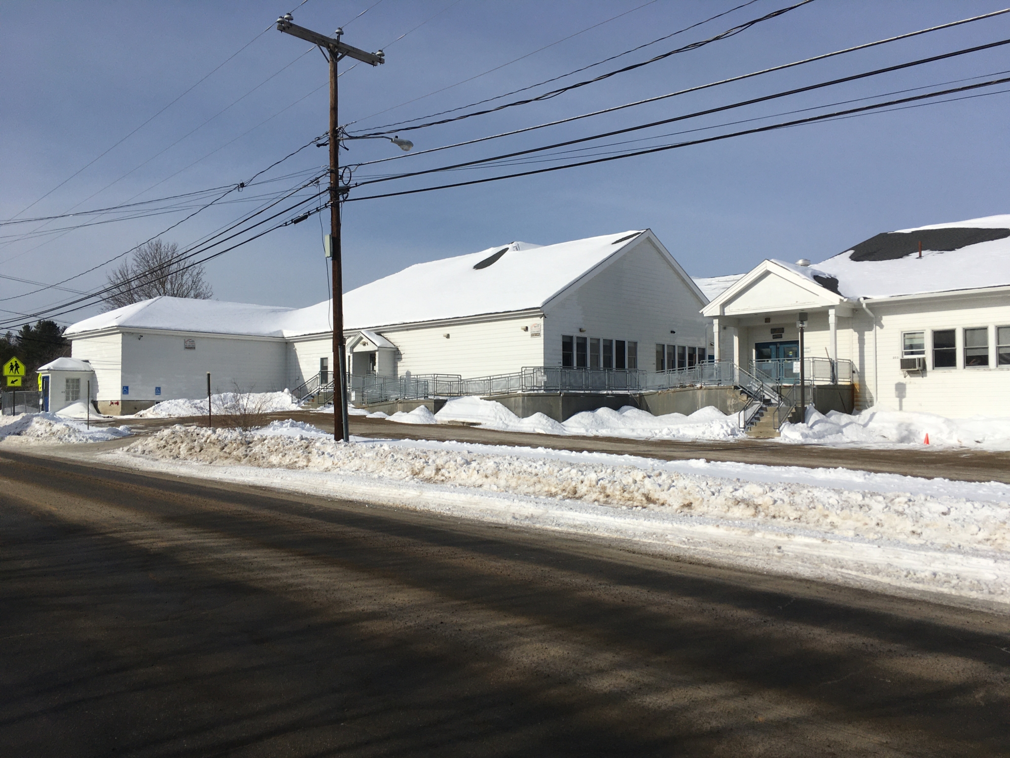 Street side view of a white sided school building on a snowy day.